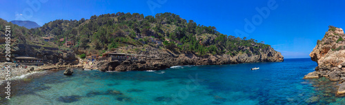 Panoramic photo of Cala Deia beach on the island of Mallorca.  The ambience is characterised by a sense of holiday relaxation and vacation. 