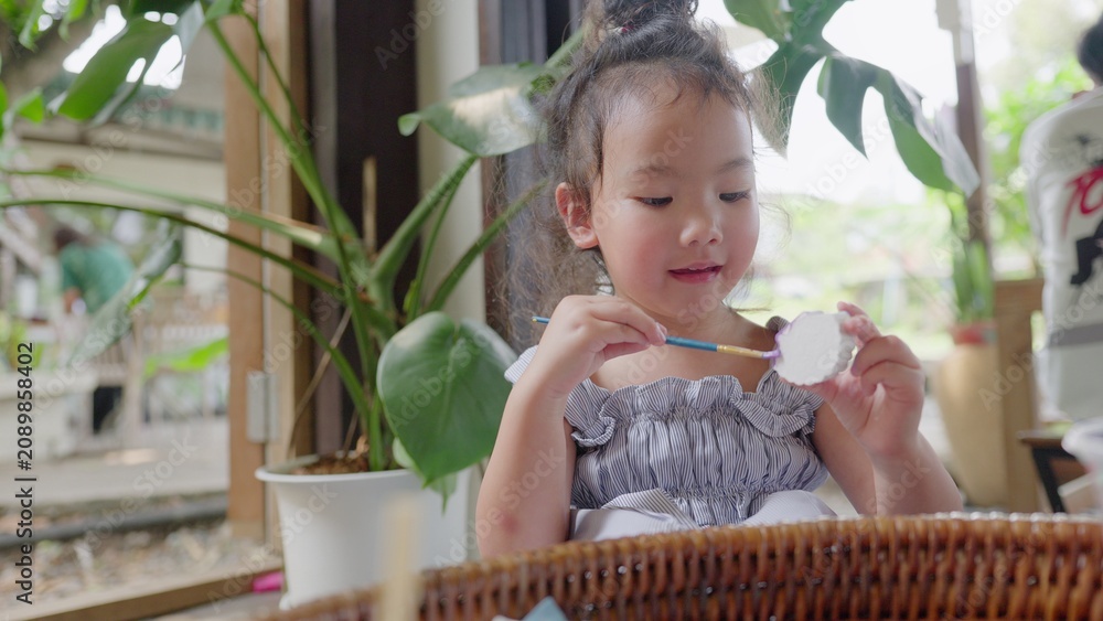 Fototapeta premium A focused young toddler girl expresses her creativity, carefully painting an art project with a brush to develop fine motor skills and enjoy learning at home.
