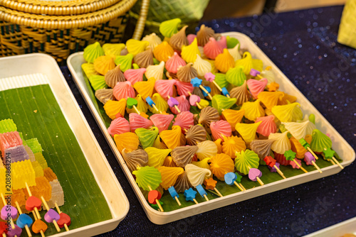 Colorful Thai traditional meringue cookies arranged on wooden sticks in a display tray, featuring vibrant pastel shades and decorative shapes at a local dessert market.