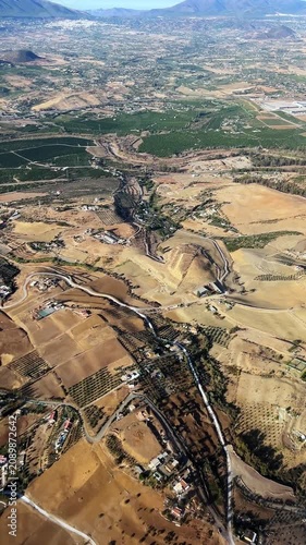 Aerial views show the landscape of Malaga Spain with fields, vineyards, and small homes. The sun shines down on the dry earth and green patches.