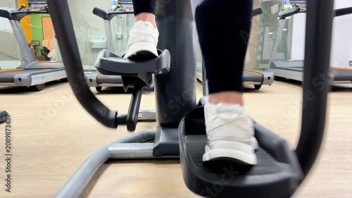 A person is working out on an elliptical machine at the gym in the afternoon. The shoes are white and the focus is on the movement of the feet