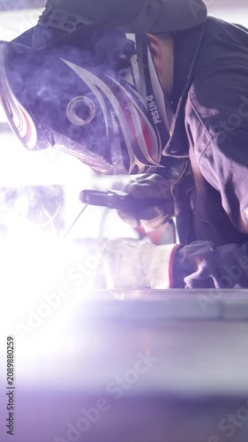 Professional welder with a protective mask and gloves welding metal parts in a workshop, sparks and smoke flying during the joining process in an industrial environment