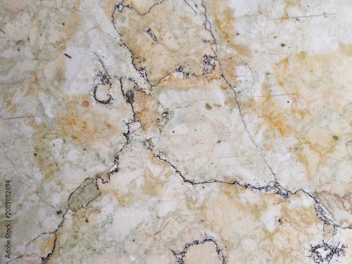 Quadro su tela Surface texture of natural marble stone with irregular crack patterns in yellowish cream color and organic black spots