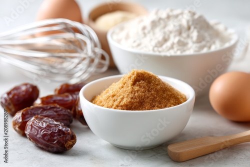 Small bowl of date sugar with whole dates flour eggs and whisk for commercial baking background and recipe banner design