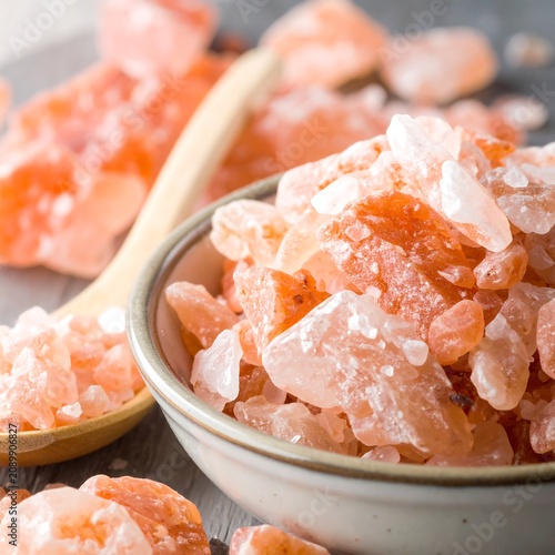 A close-up of pink crystals in a small bowl with a wooden spoon