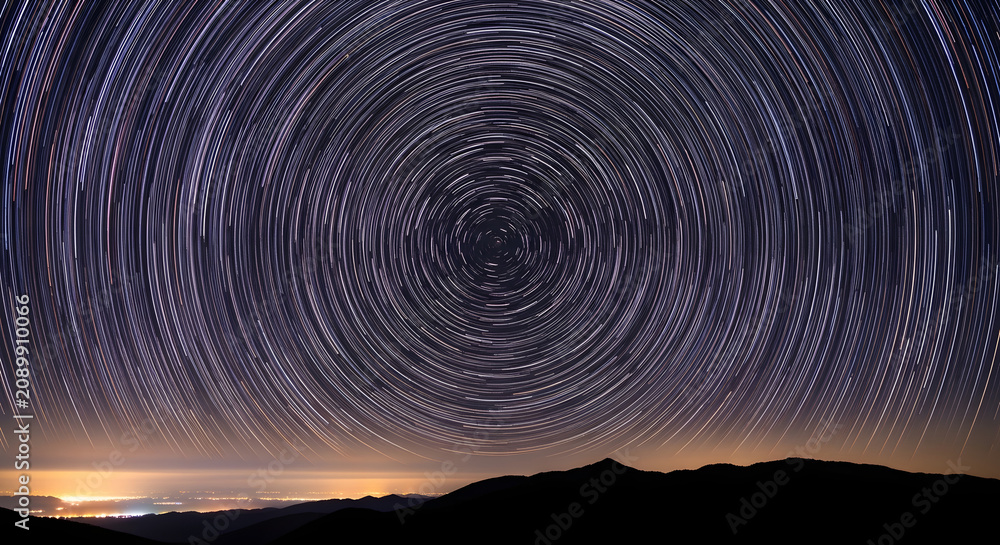 Fototapeta premium Mesmerizing Celestial Dance A Captivating Long Exposure View of Star Trails Arching Across the Night Sky Above Silhouetted Mountains