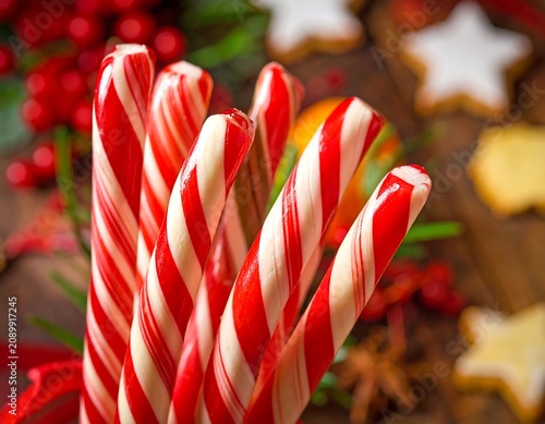 A close-up of red and white striped candy canes on a wooden table with Christmas cookies and decorations