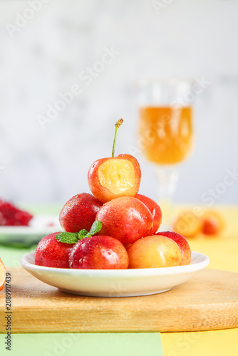 Quadro su tela Fresh Gold Chilean Rainier Cherries with Mint on White Plate and Orange Juice Ba