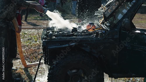 Man in dirty clothes cleans mud from off road vehicle's engine compartment with powerful stream of water. Action shot after extreme mud racing competition. Gritty, dynamic scene