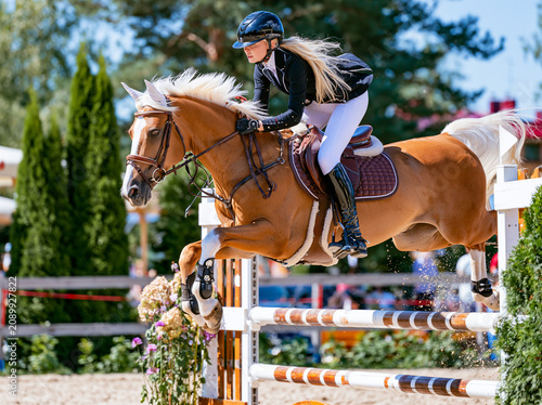 Show jumping competition, jumping over a barrier on a horse, blonde, female rider