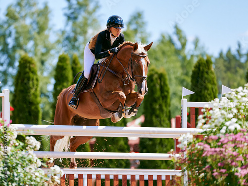 Show jumping competition, jumping over a barrier on a horse, blonde, female rider