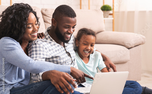 Φωτογραφία Joyful african american family of three using laptop at home together, watching