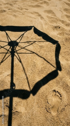 A serene coastal scene capturing the intricate shadow of a beach umbrella cast upon golden sand, accented by a single human footprint, evoking the quiet essence of a tranquil summer holiday escape.