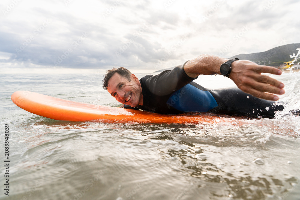 Obraz premium Middle aged sportive handsome man learning to surf, smiling in ocean water