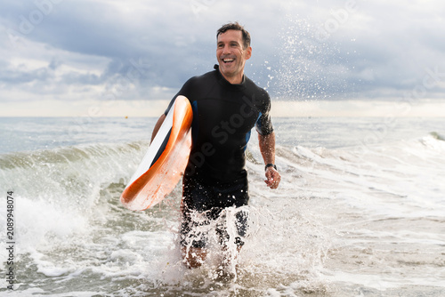 Foto Middle aged sportive handsome man learning surfing and running in the waves hold
