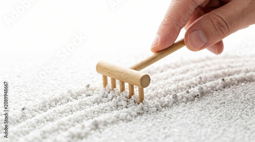 Hand using a mini bamboo rake to make lines in white gravel of a zen garden