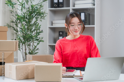 Obraz na płótnie E-commerce Success: A young, ambitious entrepreneur happily manages her online business, surrounded by packages ready for shipment