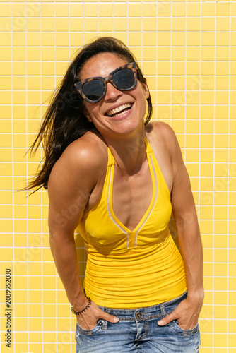 Happy beautiful asian woman wearing sunglasses and swimwear portrait  during summertime vacation - Chinese female middle aged adult looking at camera and smiling  yellow background for copyspace 