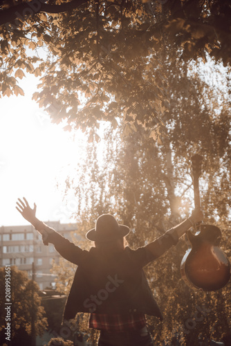 A man in a hat with long hair in a park with a guitar. Autumn atmosphere