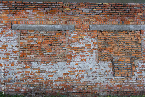 Old brick wall with bricked-up windows and peeling plaster