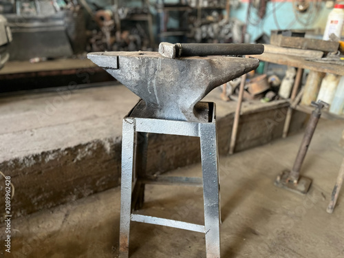 Принти на полотні In a metal workshop, a forged hammer and a traditional blacksmith’s anvil resting on a custom-made silver-colored metal table