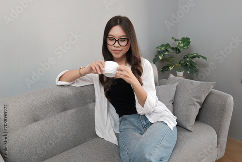 Young Asian Indonesian Woman Relaxing with Coffee While Sitting on Sofa at Home