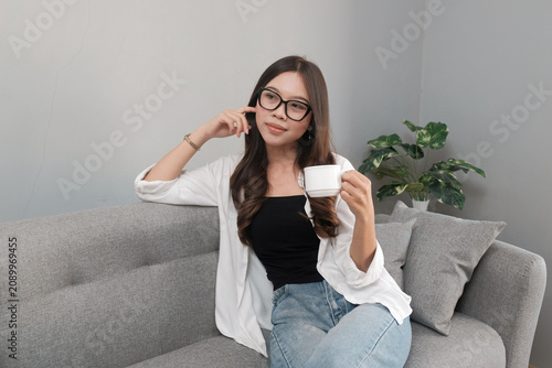 Young Asian Indonesian Woman Holding Coffee Cup and Thinking at Home