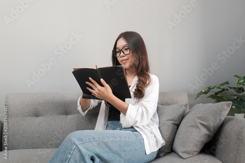 Young Asian Indonesian Woman Writing in Notebook While Relaxing on Sofa at Home