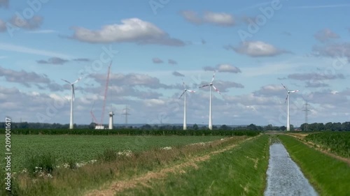 Wind farm beside agricultural fields and drainage canal - Panoramic view of a wind farm beside cultivated farmland and a drainage canal under a bright summer sky. Renewable energy, sustainable land us