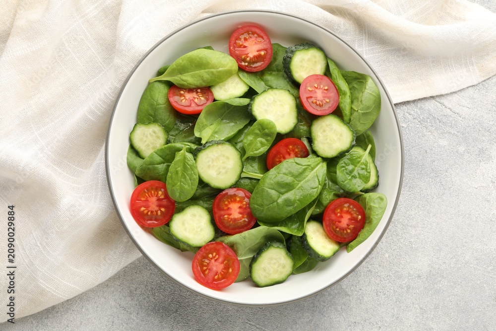 Naklejka premium Appetizing salad with spinach, tomatoes and cucumbers served on grey table, top view