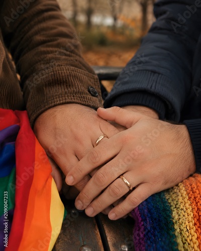 Gay men holding hands showing wedding rings outdoors