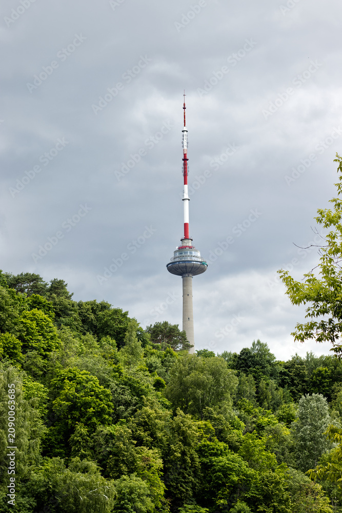 Obraz premium Vilnius, Lithuania June 11, 2026, Vilnius TV Tower rising above a lush green forest on a cloudy summer day