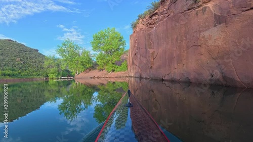 Relaxing POV kayaking through the scenic sandstone canyons of Horsetooth Reservoir in Fort Collins, Colorado. Peaceful summer morning paddle on calm water with the bow of a carbon fiber kayak.