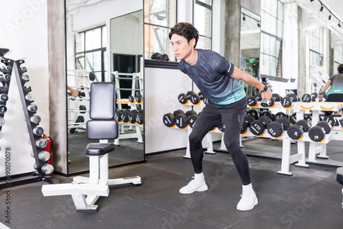 Schilderij op canvas Young man doing dumbbell tricep kickbacks in modern gym