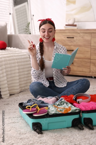 Packing suitcase for trip. Woman with notebook checking her belongings on floor at home