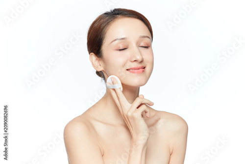 Young woman applying foundation with cosmetic puff on white background