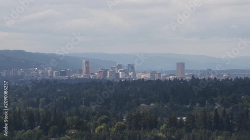 Aerial Portland cityscape viewed over forested valley in Clackamas County Oregon with skyscrapers on cloudy summer day