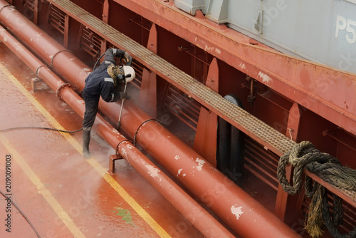 Fotografía operating a high-pressure hydro blaster on cargo ship conduit lines to remove de