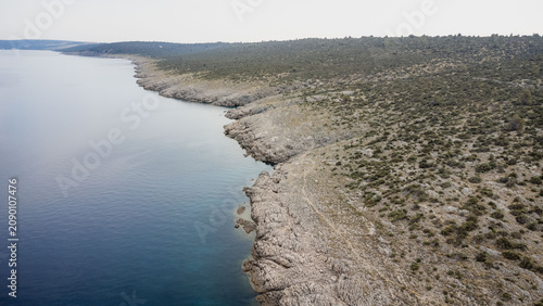 Canvastavla High altitude aerial view of rocky coastline meeting calm blue sea, sparse scrub