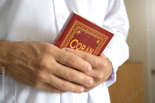 Person wearing white holding a holy coran book, symbolizing islam and devotion