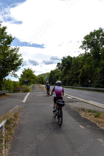 Two cyclists riding along a dedicated bicycle path through the scenic Rhine Valley in Germany. Active travel, sustainable transportation and outdoor recreation in a picturesque European landscape.