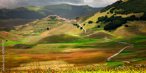 Fotografi A small village sits atop a rolling green hill in a vast valley