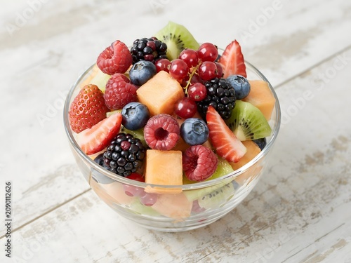 Fresh fruit salad in glass bowl on rustic wooden table