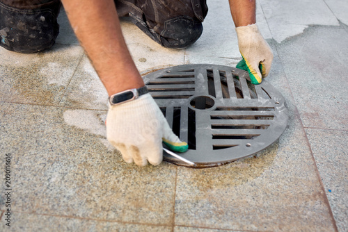 man cleaning drain cover on outdoor pavement with sponge, neutral mood, close-up view, for cleaning services and maintenance, gray and green tones, natural light, modern andd.