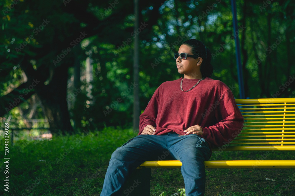 Obraz premium Young man wearing sunglasses sitting on a park bench. Man wearing sunglasses sitting in the park