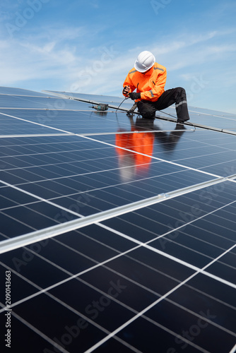 Technician installing solar panels on factory roof for green energy. A skilled technician in safety gear is working on a solar panel installation on rooftop.
