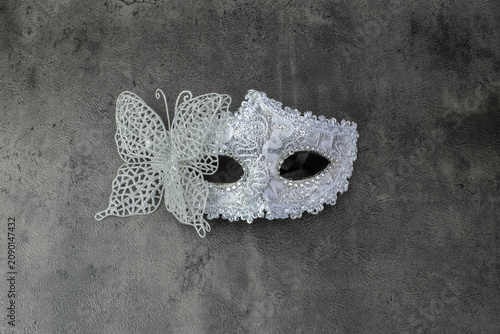 A silver lace masquerade mask with butterfly detail is photographed from above on a dark textured surface. Suitable for party mask, carnival accessory, Halloween costume, masquerade decoration