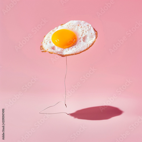 Surreal pop art concept of fried egg floating like balloon on pink background