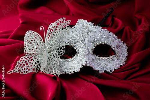 A silver masquerade mask with lace butterfly detail rests on red satin fabric. Suitable for carnival party, masquerade ball, Halloween costume, mystery theme