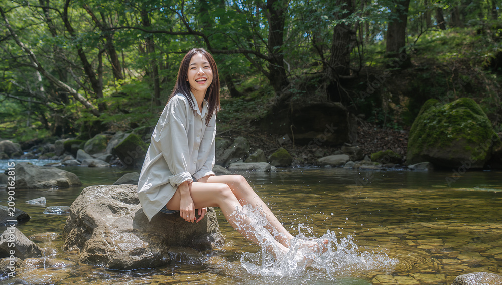 Fototapeta premium 冷たい清流の岩場に腰掛けて水遊びをしながら笑うシャツ姿の日本人女性